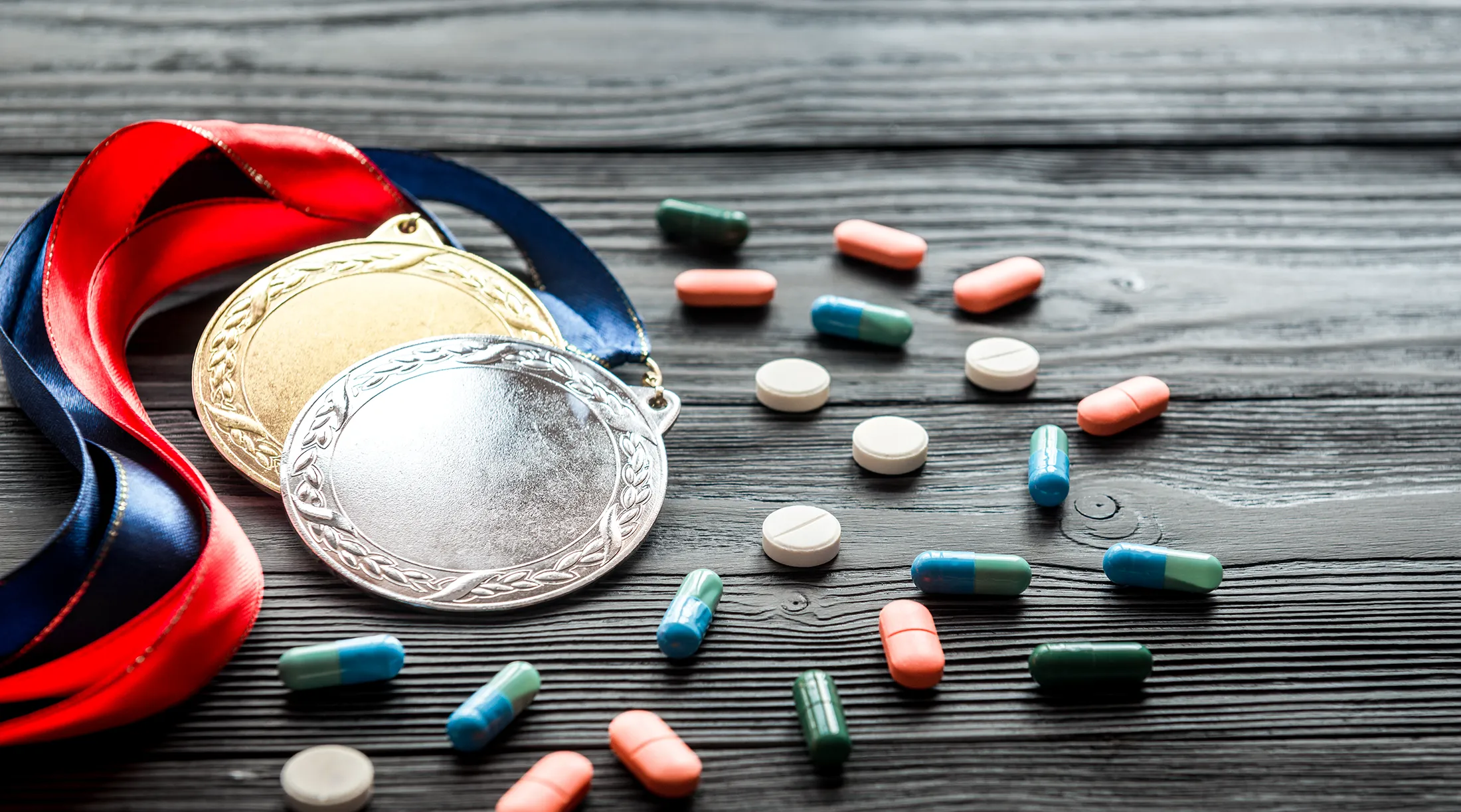 Titelbild zur Anti-Doping Aufklärung - ein paar medaillen liegen neben Pillen und Tabletten auf einem hölzernen Tisch